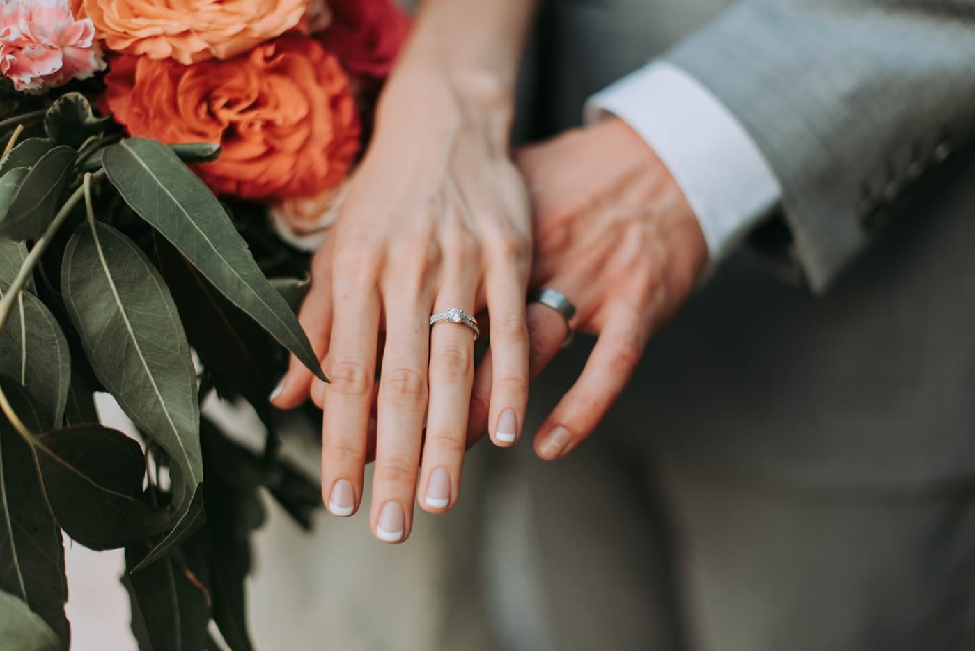 Two hands wearing wedding bands, resting on eucalyptus leaves